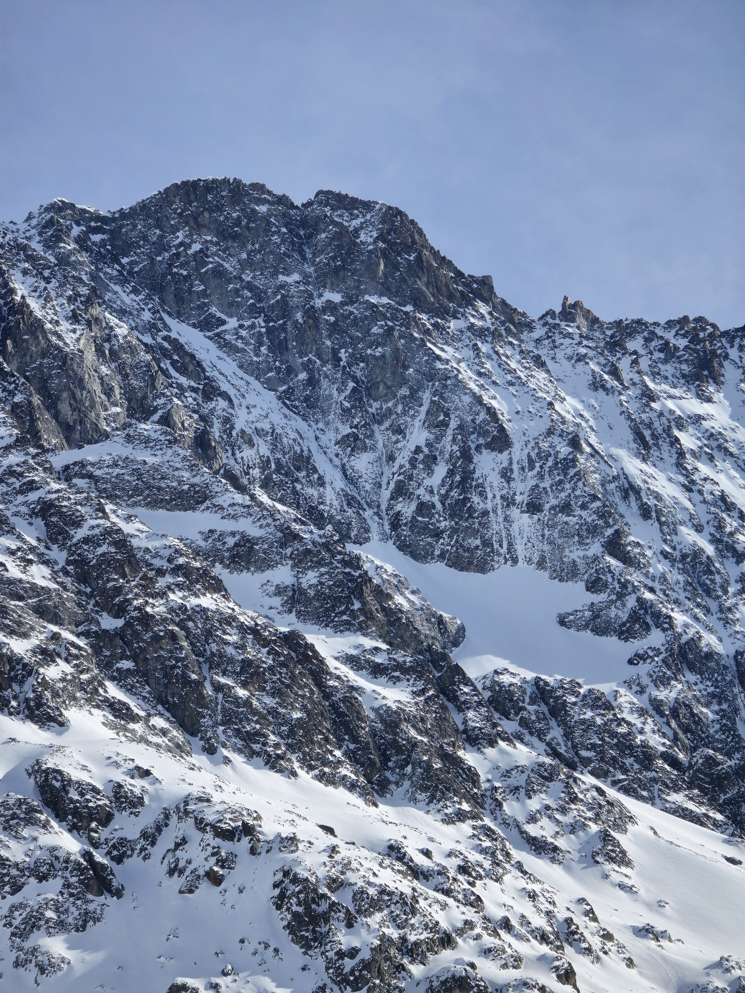 Grande face rocheuse striée de neige sous un ciel clair, vue depuis la descente du deuxième jour du Tour des Agneaux (Écrins)