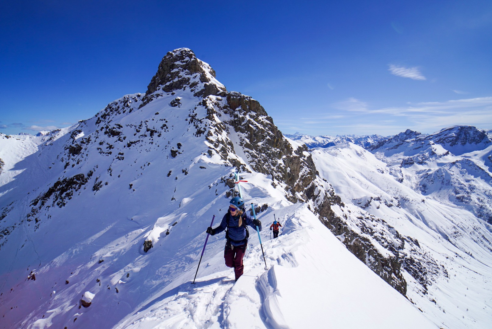 Skieur de randonnée sur une crête enneigée, devant un sommet rocheux sous un ciel bleu, Tour des Agneaux (Écrins)