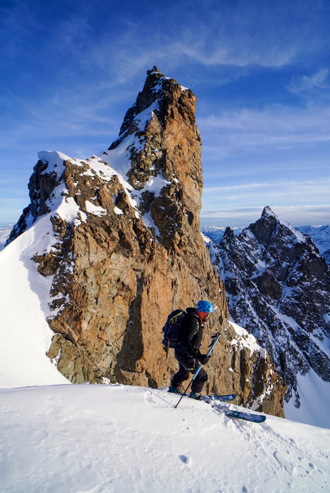 Skieur à pied au pied d'une aiguille rocheuse ocre sur une arête enneigée, Tour des Agneaux (Écrins)