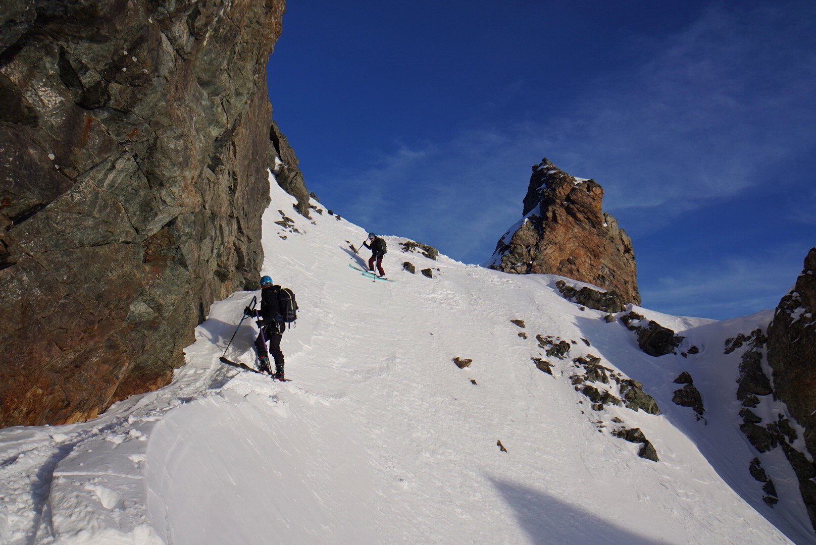 Skieurs franchissant un passage entre des rochers, une aiguille rocheuse en arrière-plan, Tour des Agneaux (Écrins)