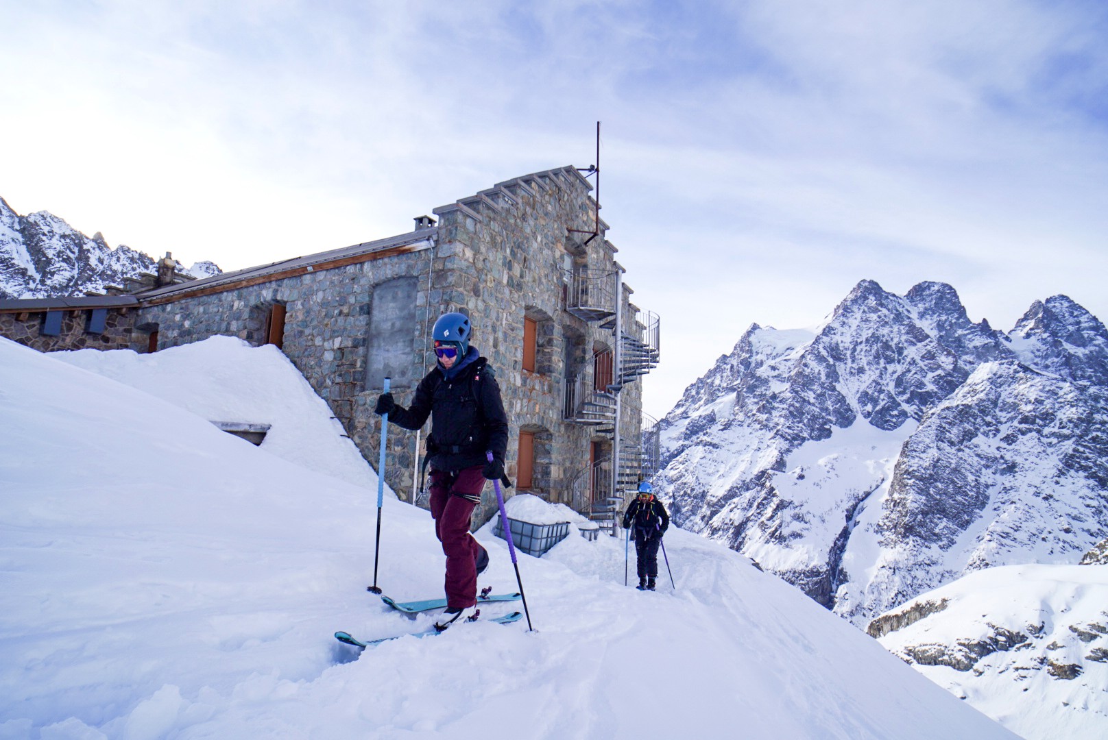 Skieurs devant un grand refuge en pierre, avec un sommet glaciaire en arrière-plan, Tour des Agneaux (Écrins)