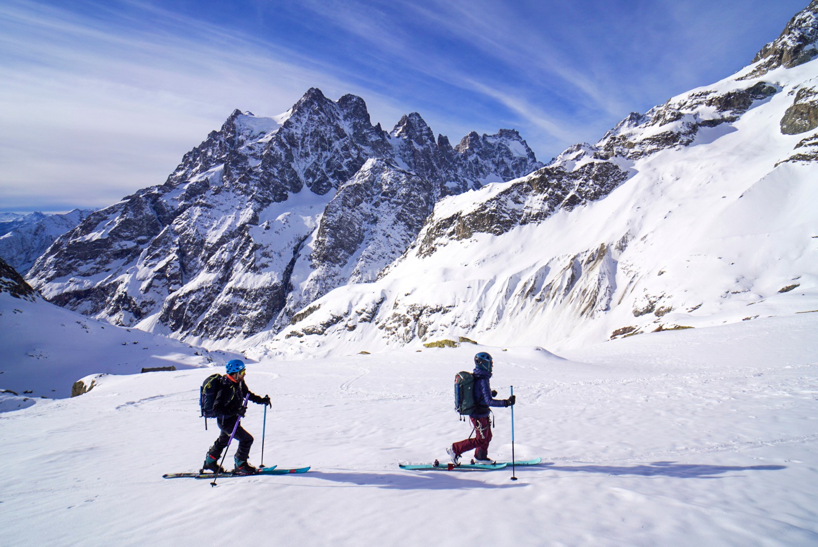 Deux skieurs de randonnée sur un vaste glacier enneigé, dominé par un massif rocheux, Tour des Agneaux (Écrins)