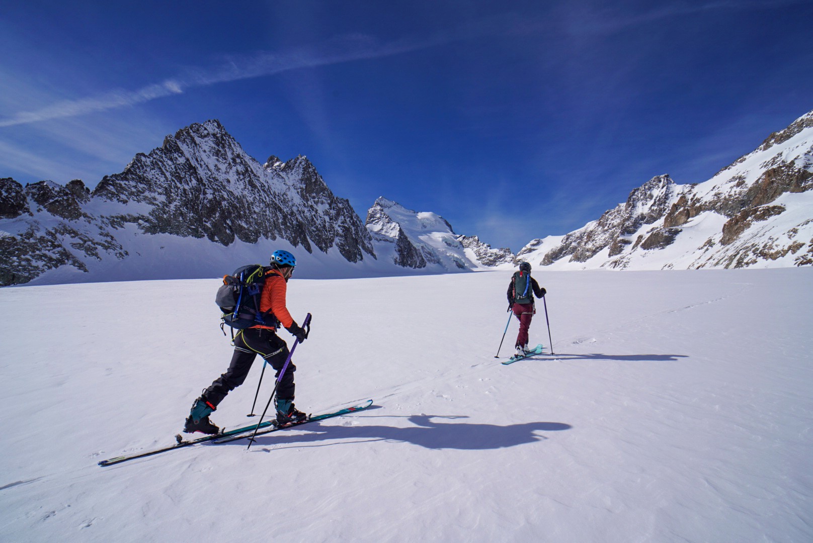 Skieurs de randonnée sur un plateau glaciaire, face à des sommets enneigés sous un ciel bleu profond, Tour des Agneaux (Écrins)