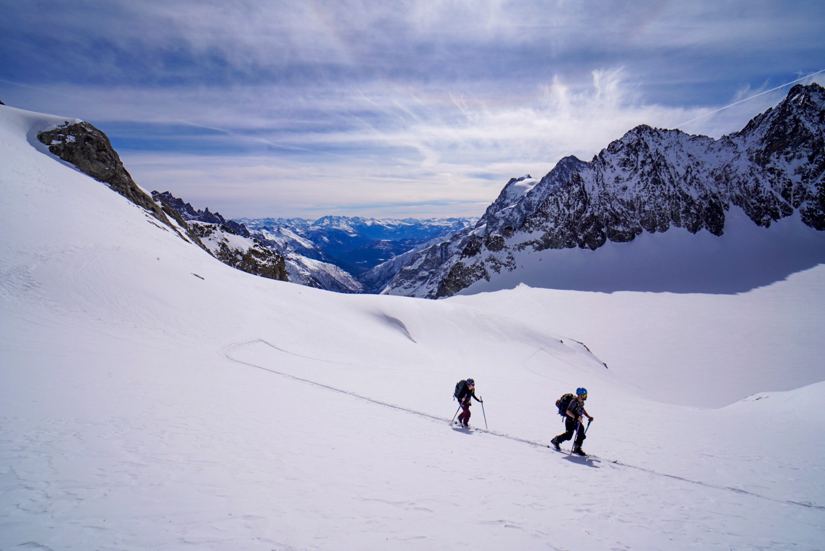 Deux skieurs de randonnée en montée sur un glacier, avec une vallée visible au loin, Tour des Agneaux (Écrins)