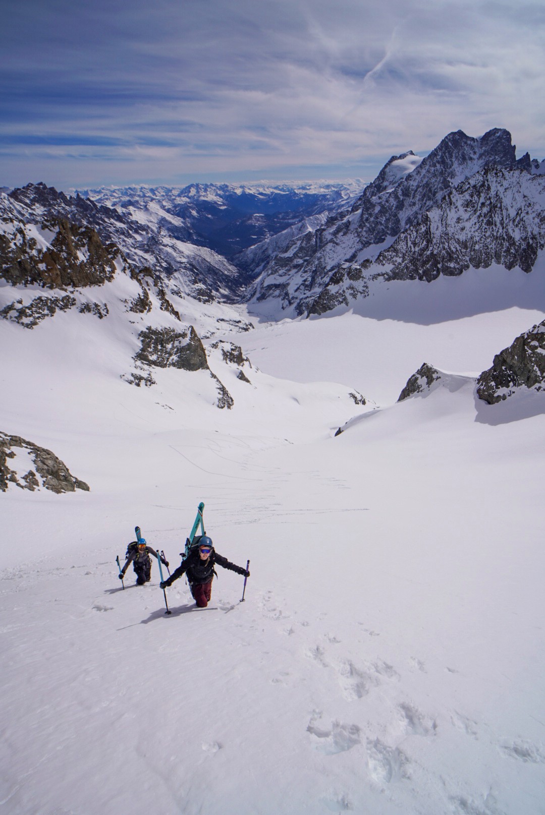 Deux skieurs de randonnée en montée sur une pente enneigée, avec une vallée en arrière-plan, Tour des Agneaux (Écrins)