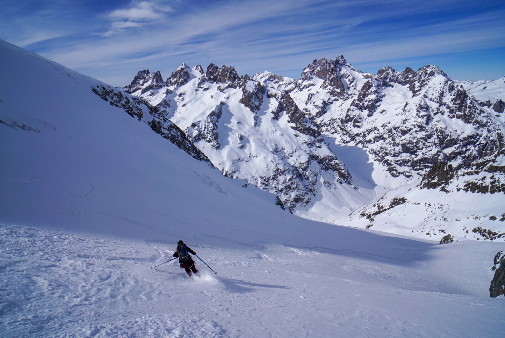 Skieur descendant une grande pente de neige face à un massif de sommets rocheux, Tour des Agneaux (Écrins)