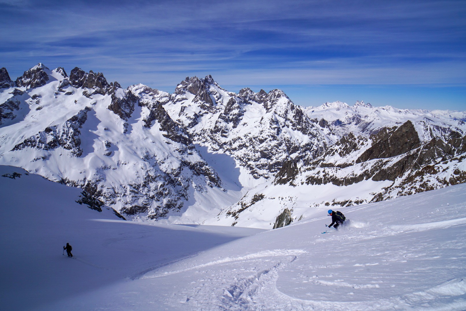 Deux skieurs descendant un vaste vallon glaciaire face à une chaîne de sommets, Tour des Agneaux (Écrins)