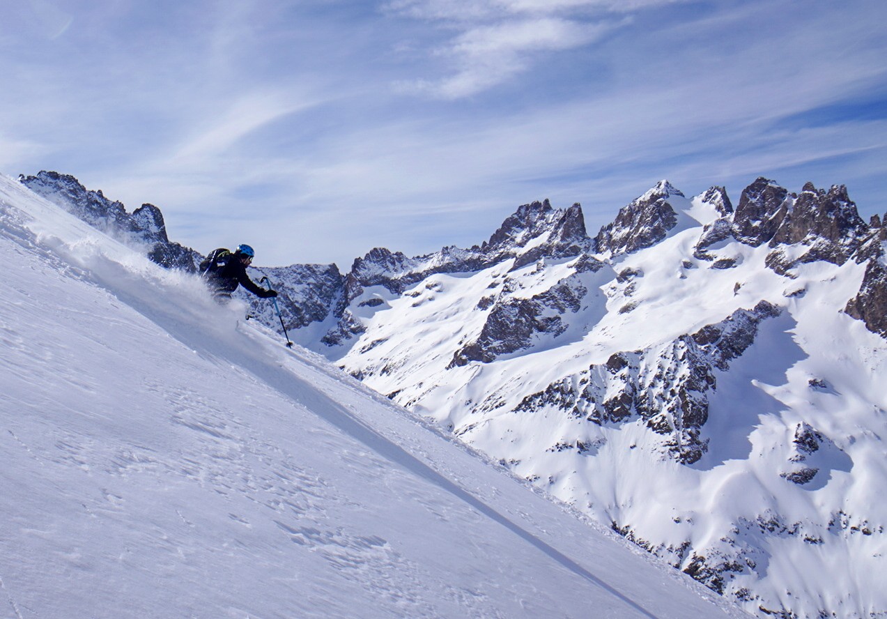 Skieur dans un nuage de poudreuse sur une pente raide, face à une paroi rocheuse, Tour des Agneaux (Écrins)