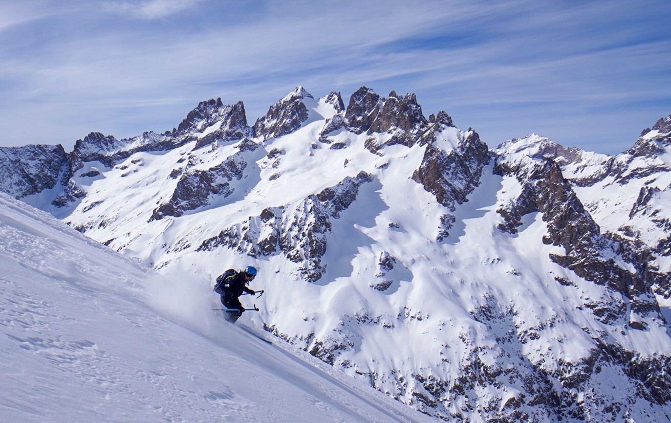 Skieur en descente dans la poudreuse devant une grande face rocheuse enneigée, Tour des Agneaux (Écrins)