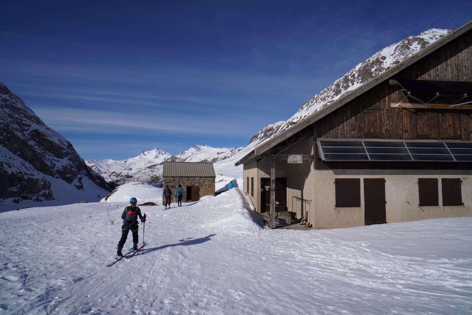 Skieur devant un chalet de montagne et une petite cabane, près de l'Alpe de Villar-d'Arêne (Tour des Agneaux, Écrins)