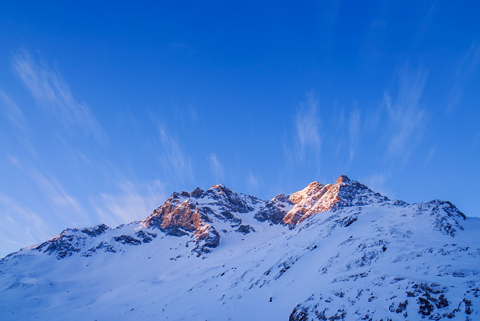Sommets enneigés éclairés par les premières lueurs orangées du matin, sous un ciel bleu strié de nuages, Tour des Agneaux (Écrins)