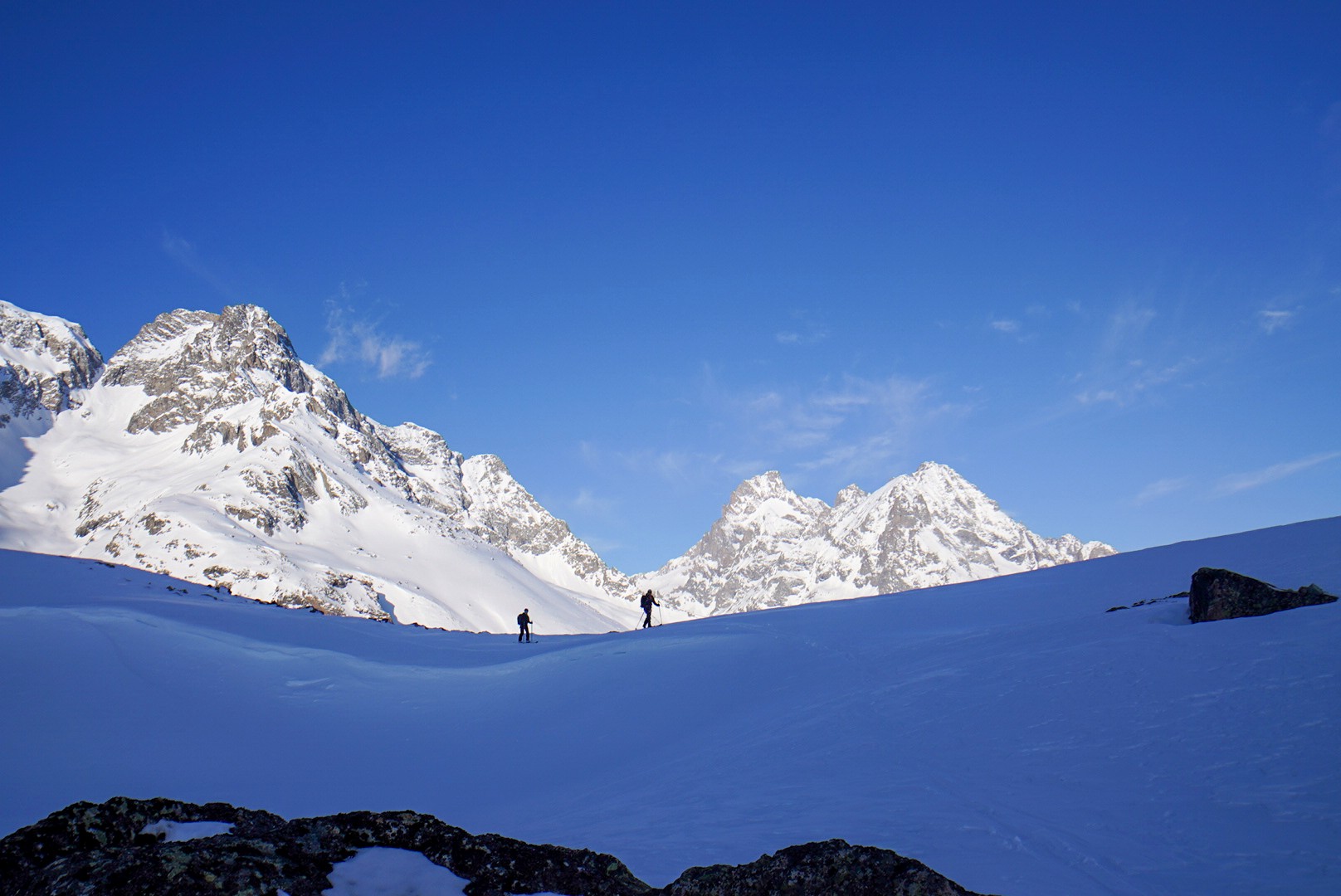 Deux skieurs au loin sur un grand plateau enneigé, au pied de sommets glaciaires, Tour des Agneaux (Écrins)