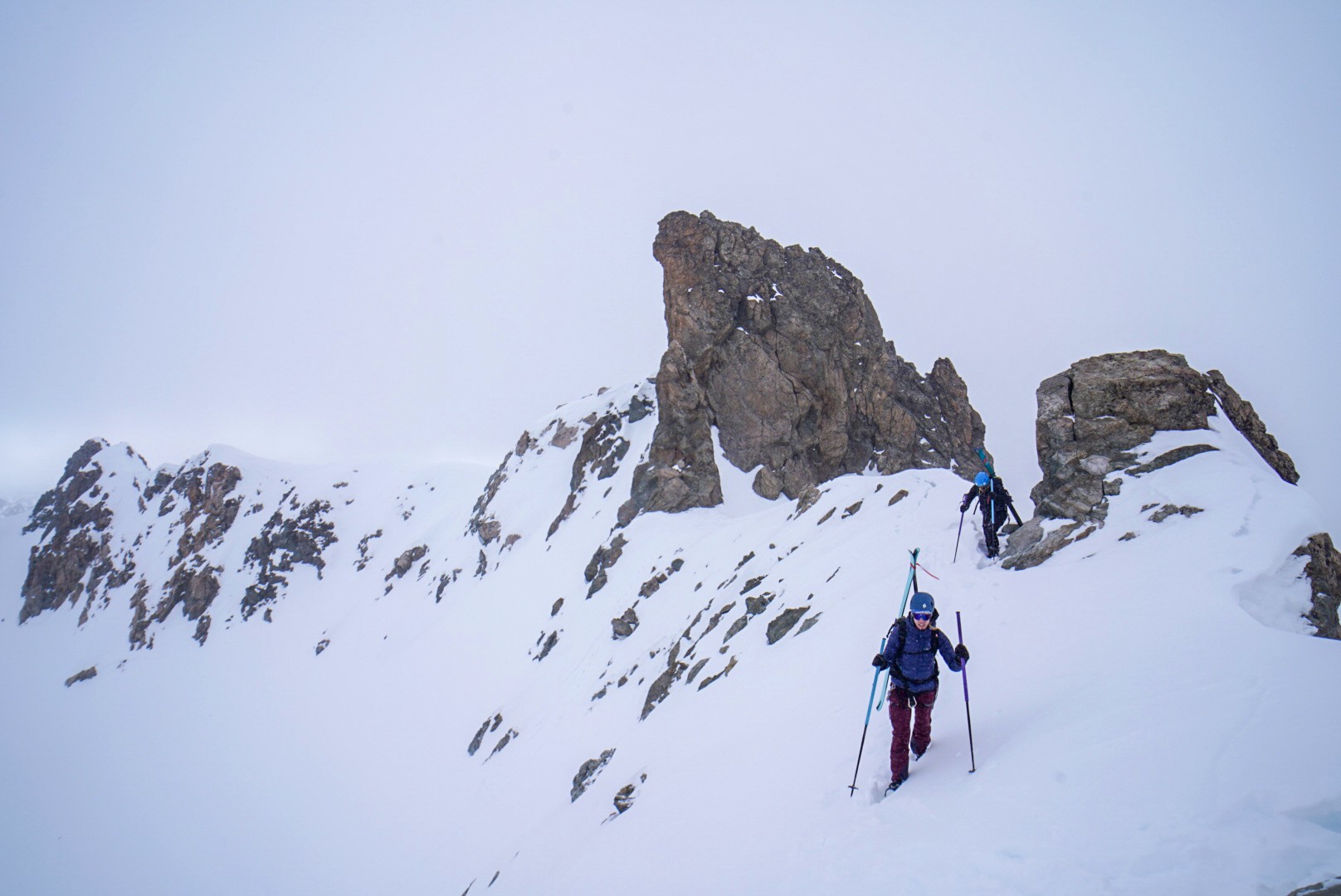 Skieurs sur une crête enneigée, devant une aiguille rocheuse dans la brume, Tour des Agneaux (Écrins)