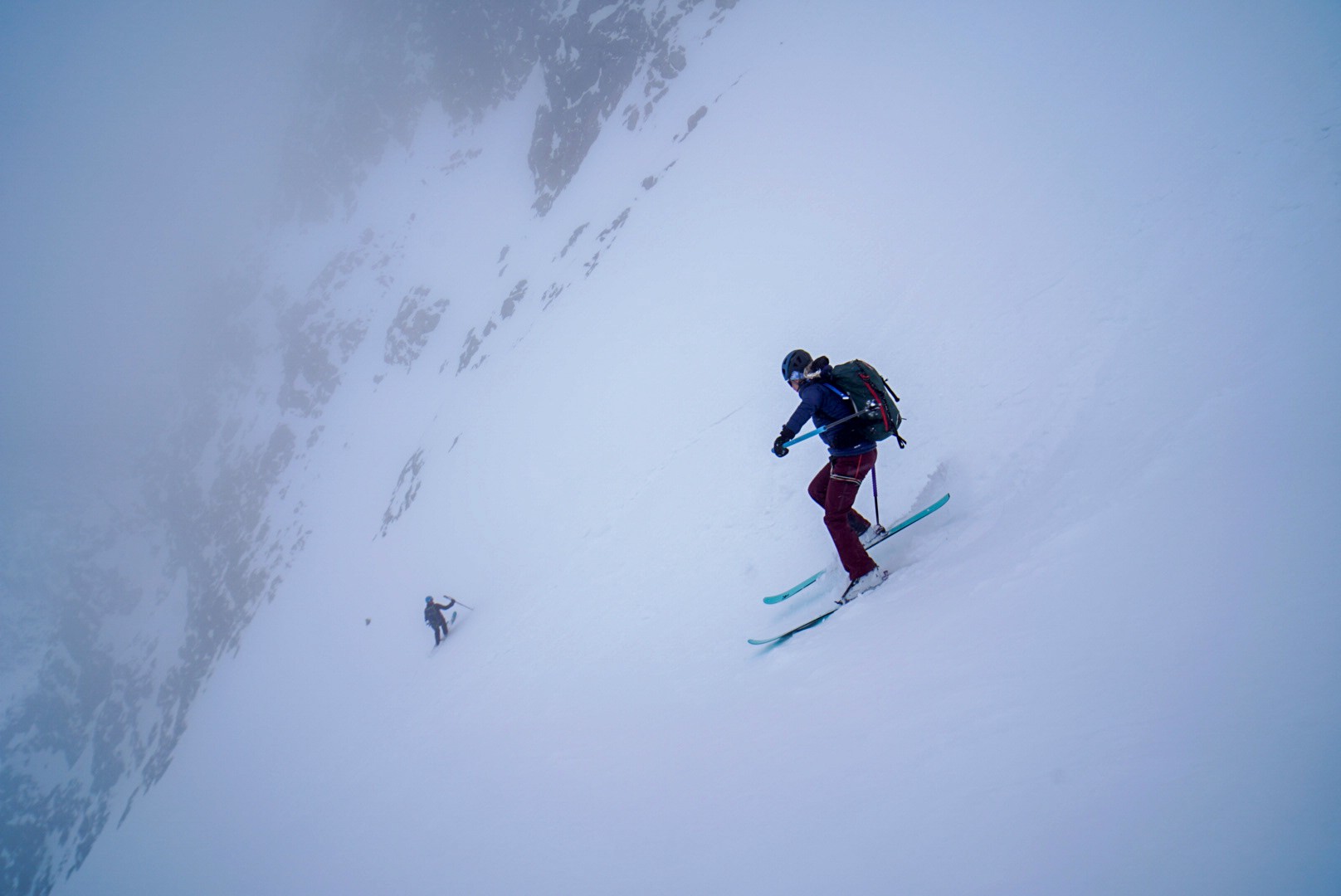 Skieur dans un couloir enneigé étroit bordé de rochers, un autre skieur plus bas, dans la brume, Tour des Agneaux (Écrins)