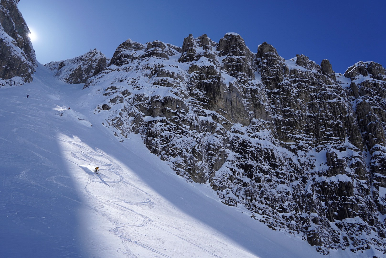 Descente au soleil sous les barres rocheuses pendant la traversée à ski des Alpes ligures, au jour 2 de l’itinérance.
