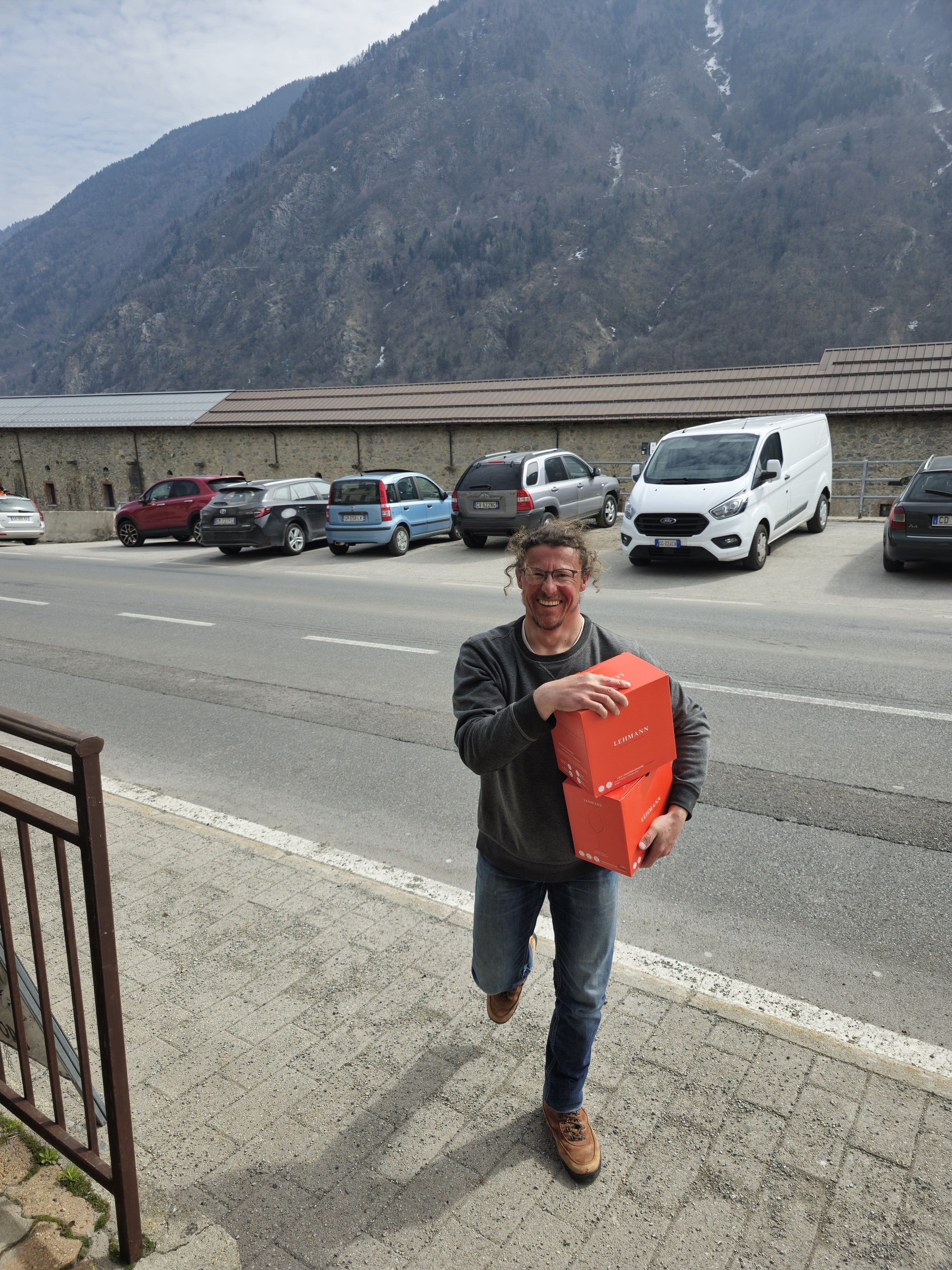 homme portant des coffrets de vin dans une rue de montagne, Vinadio