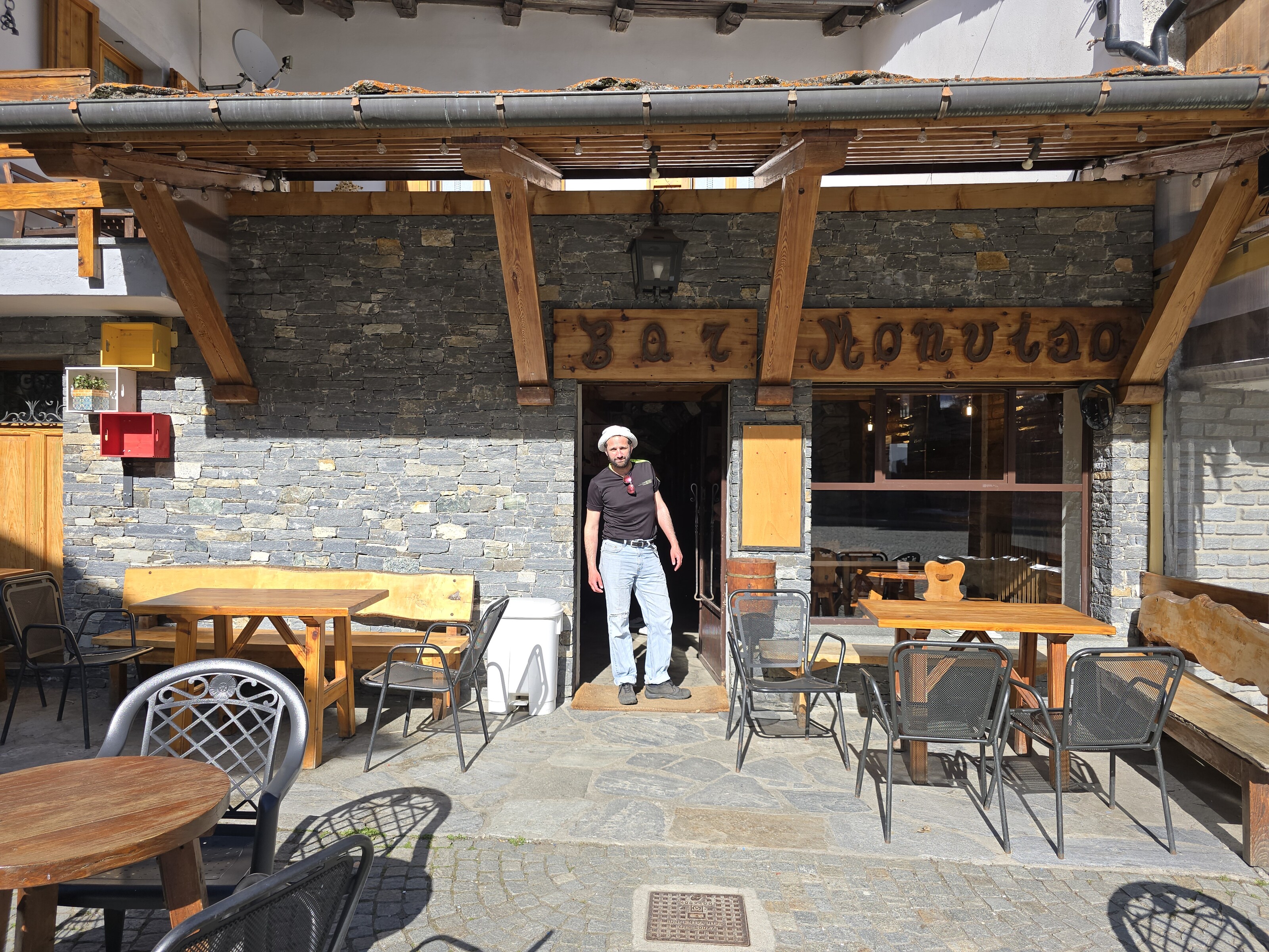 homme debout devant la façade en pierre d'un bar de montagne, Pontechianale
