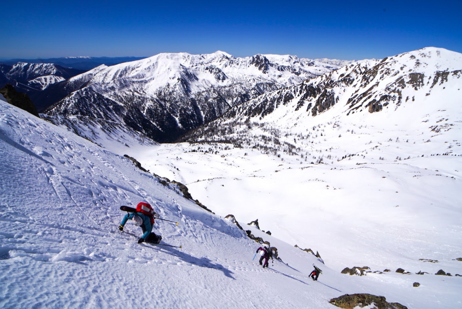 Skieur en portage sur une pente raide, panorama sur les vallées du Mercantour