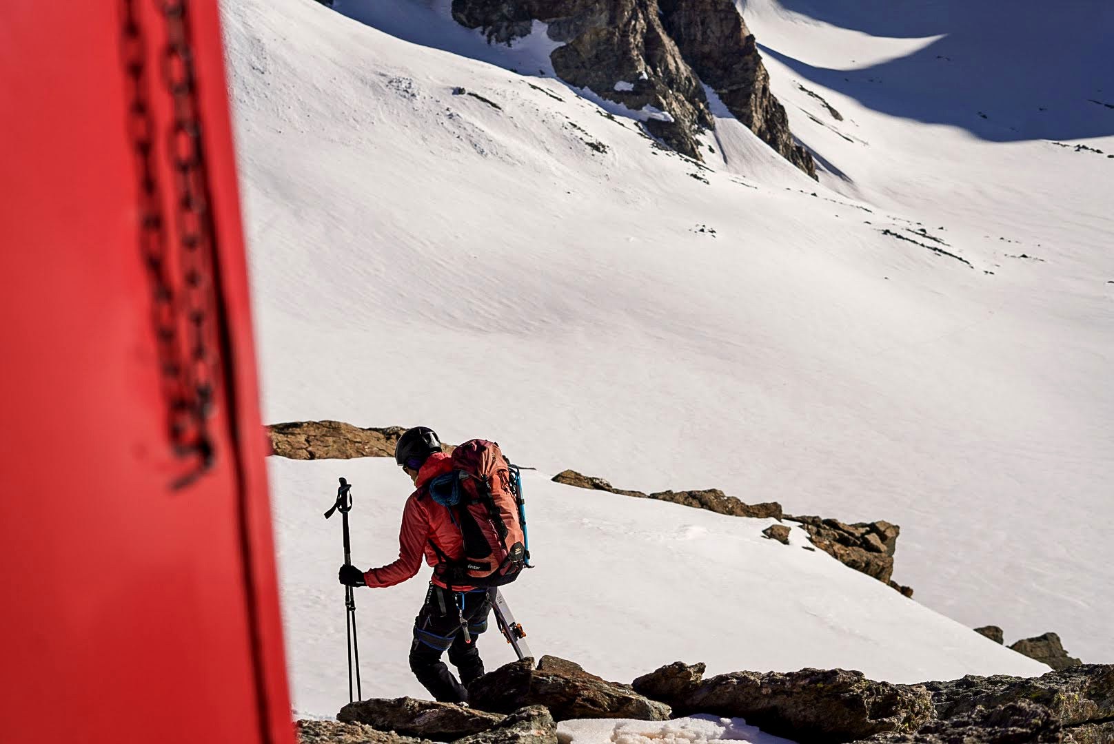 Un alpiniste sort du bivouac rouge, skis sur le sac.