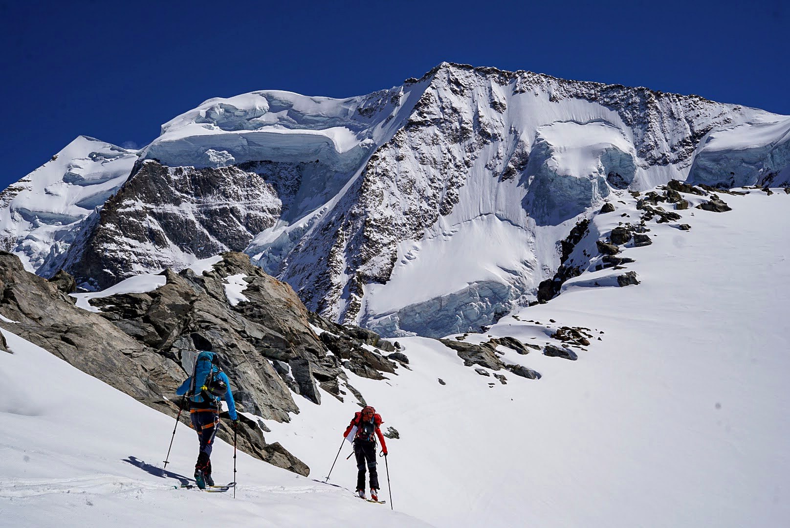 Deux skieurs évoluent encordés devant les sommets glaciaires.