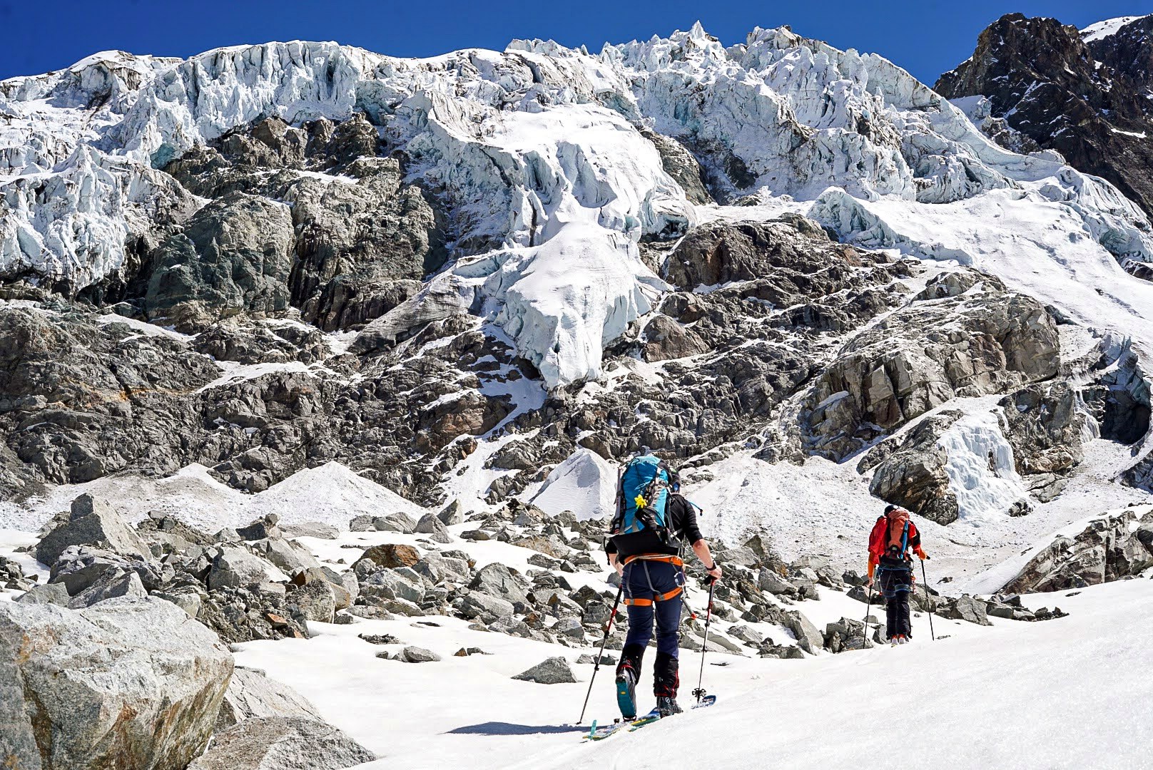 Deux alpinistes à skis passent au pied d’un chaos de séracs.