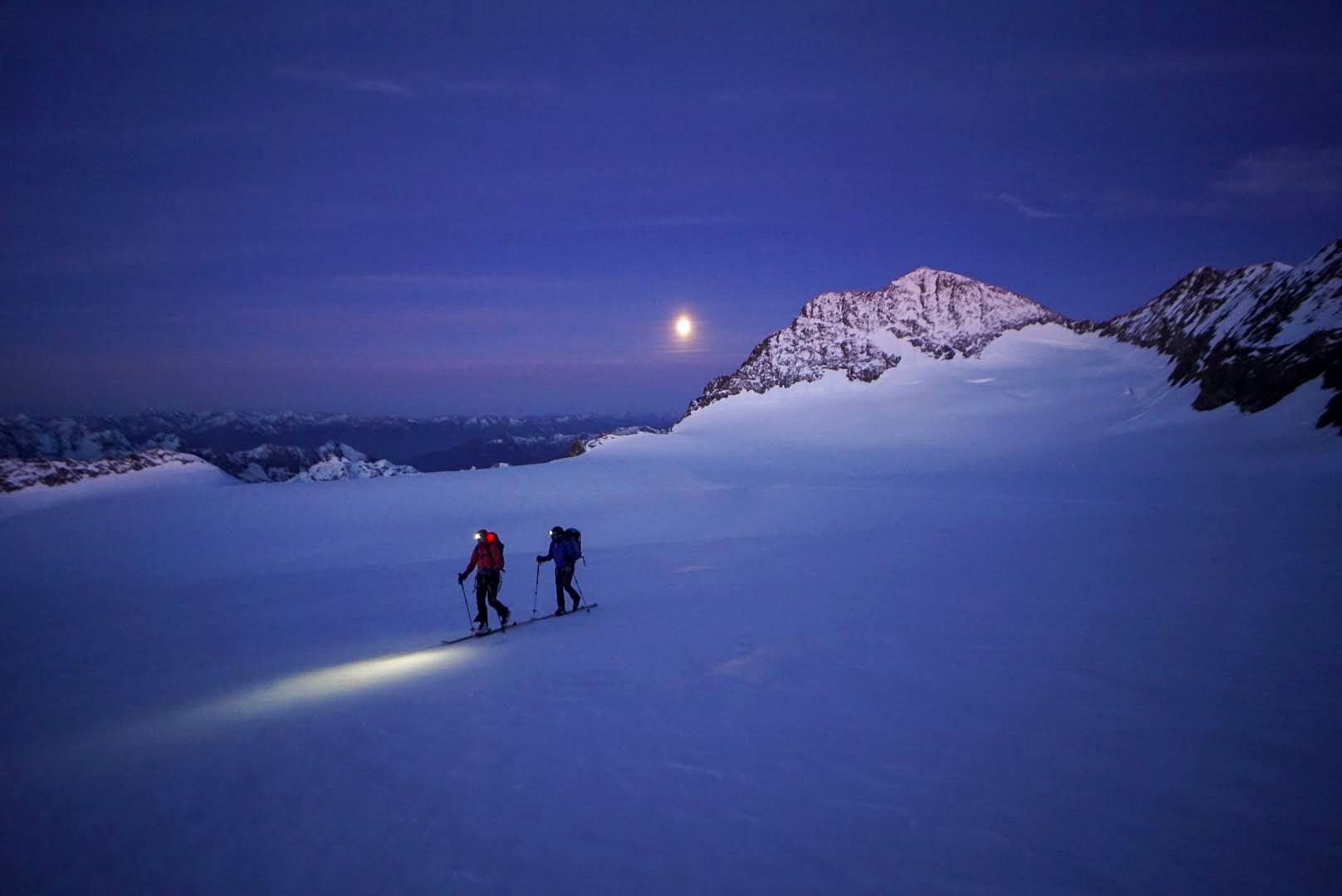 Deux skieurs remontent une pente enneigée à la lueur de leurs frontales.
