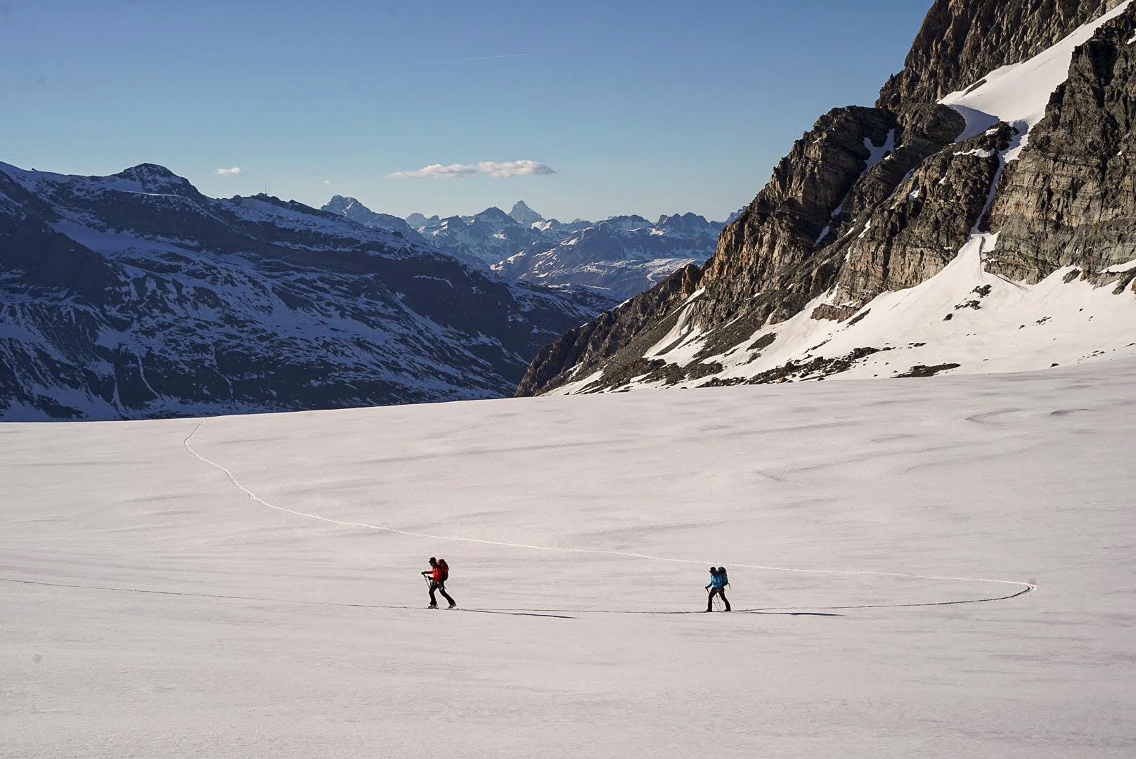 Deux skieurs progressent sur la neige au pied de hautes parois.