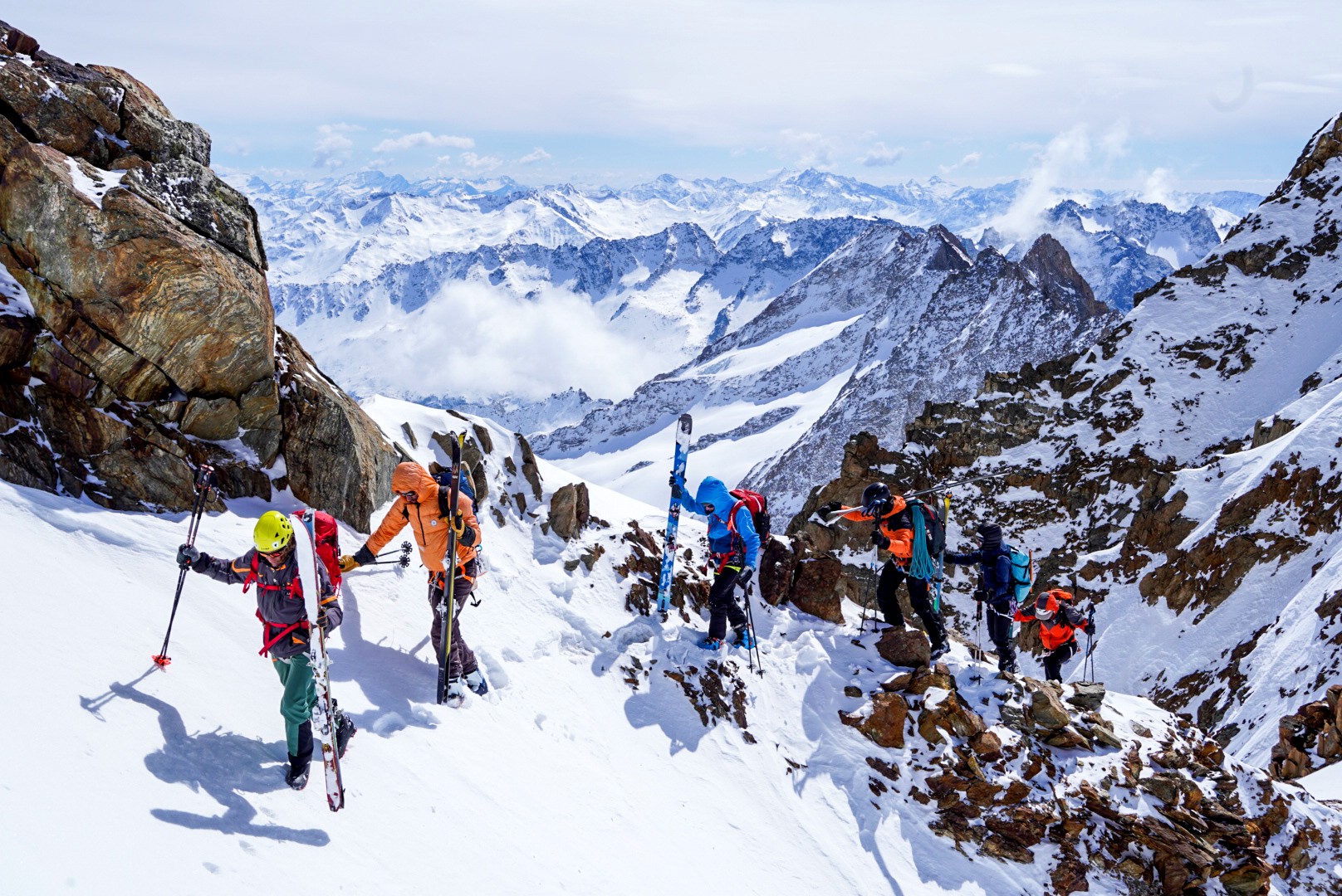 Skieurs réunis sur un col rocheux face à un panorama de montagnes et de nuages, Dammastock