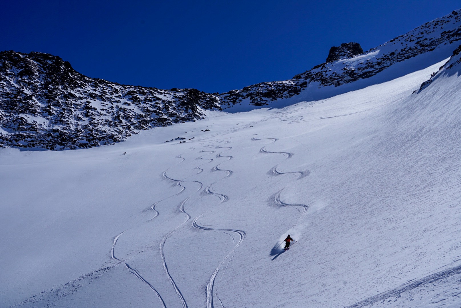Skieur en pleine descente dans la poudreuse, traces sinueuses derrière lui, Dammastock