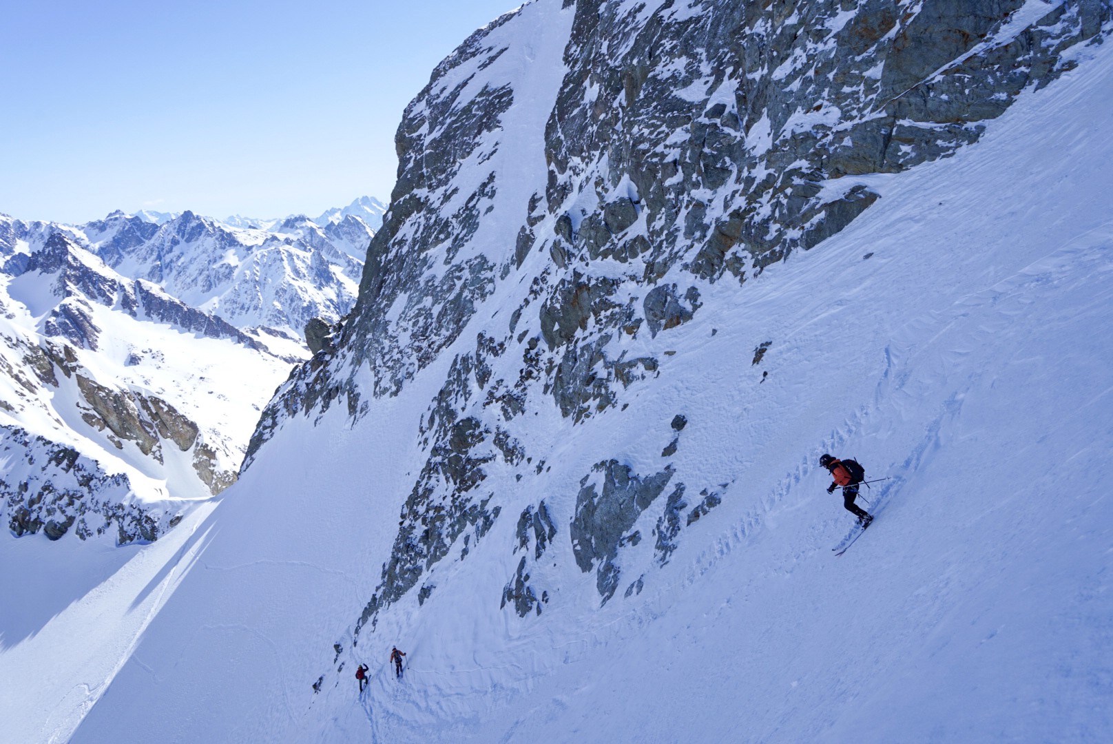 Skieur descendant une pente raide sous une grande paroi rocheuse, Dammastock