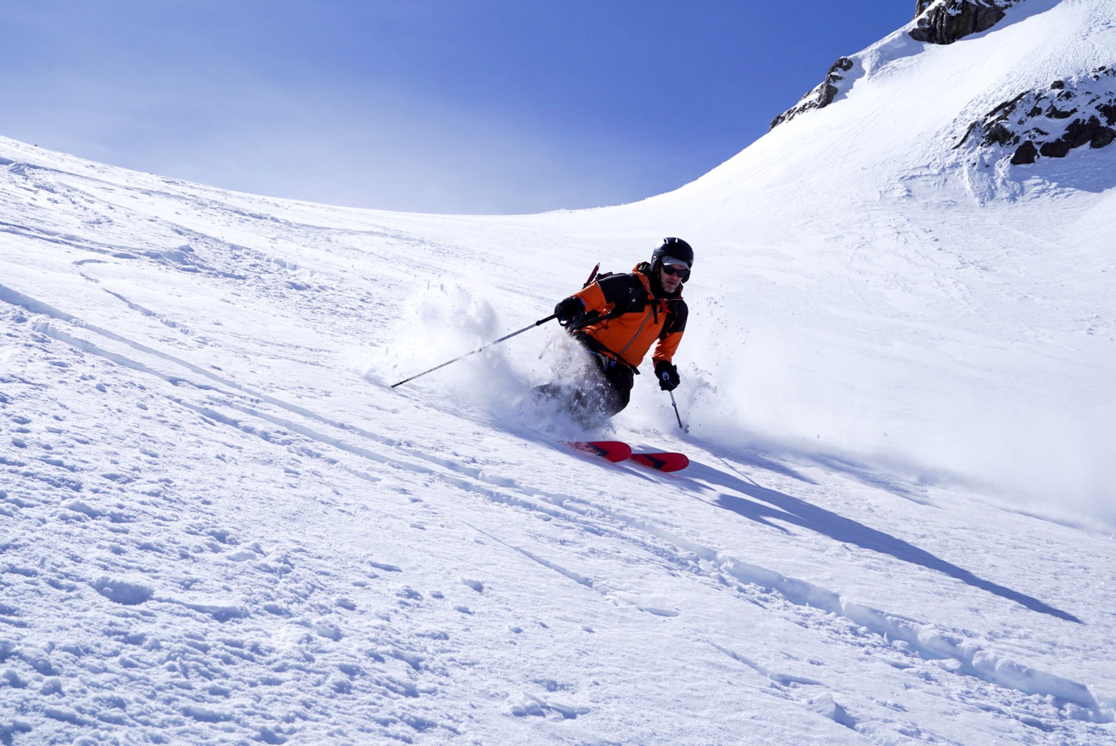 Skieur au sac orange dans la poudreuse d'une large pente ensoleillée, Dammastock