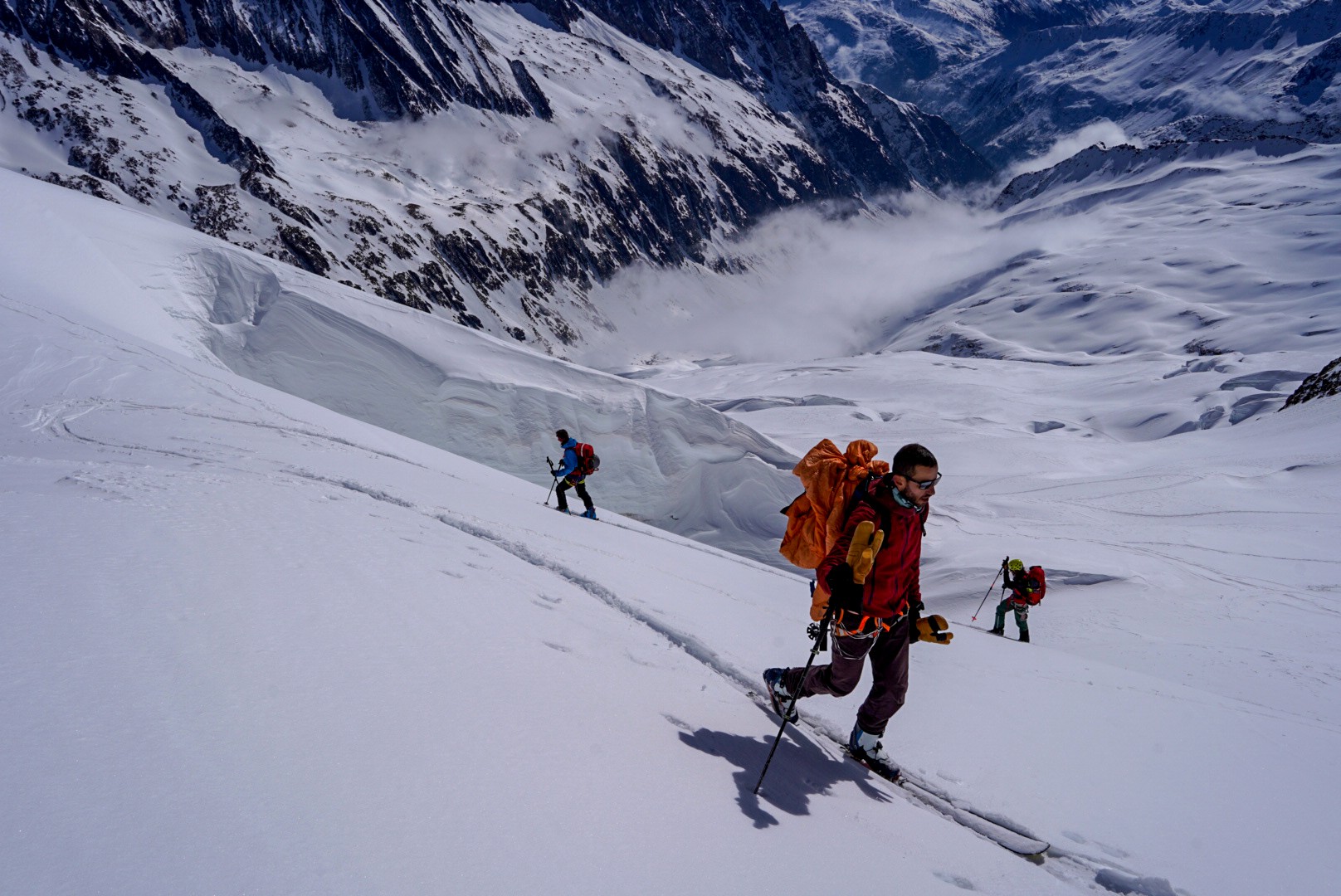 Skieur au sac orange longeant une crevasse sur un glacier, vaste vallée en contrebas, Dammastock