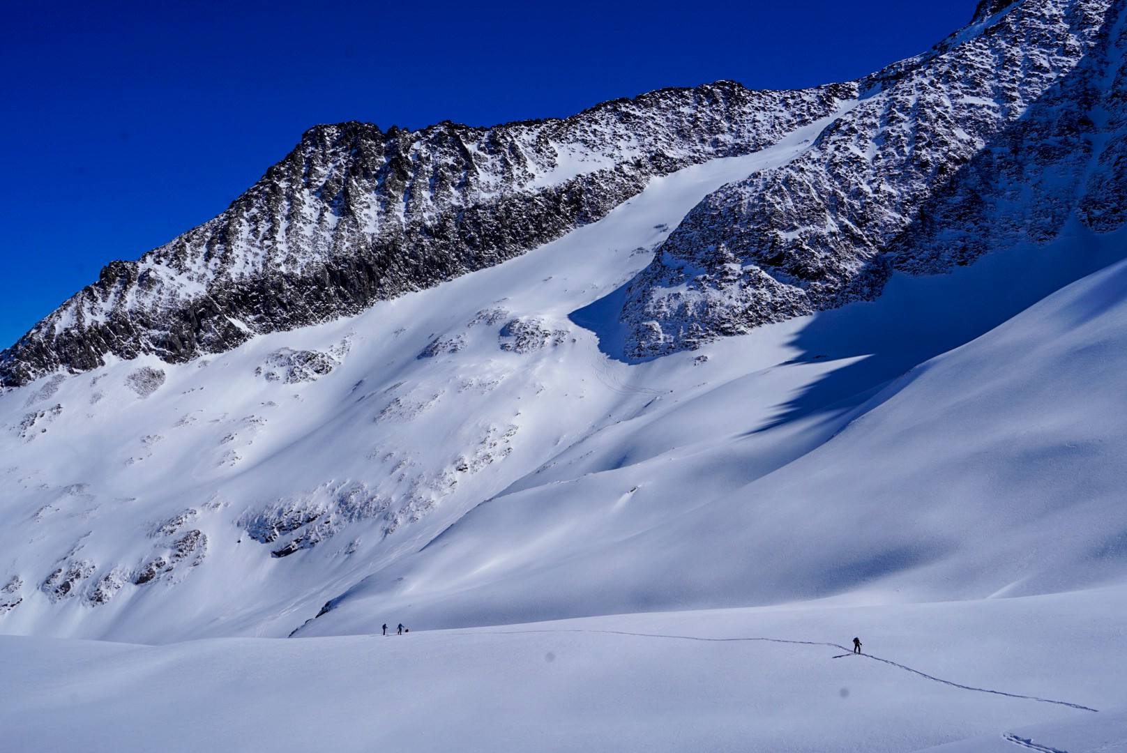 Petite cordée de skieurs sur un glacier au pied de grandes parois rocheuses sombres, Dammastock