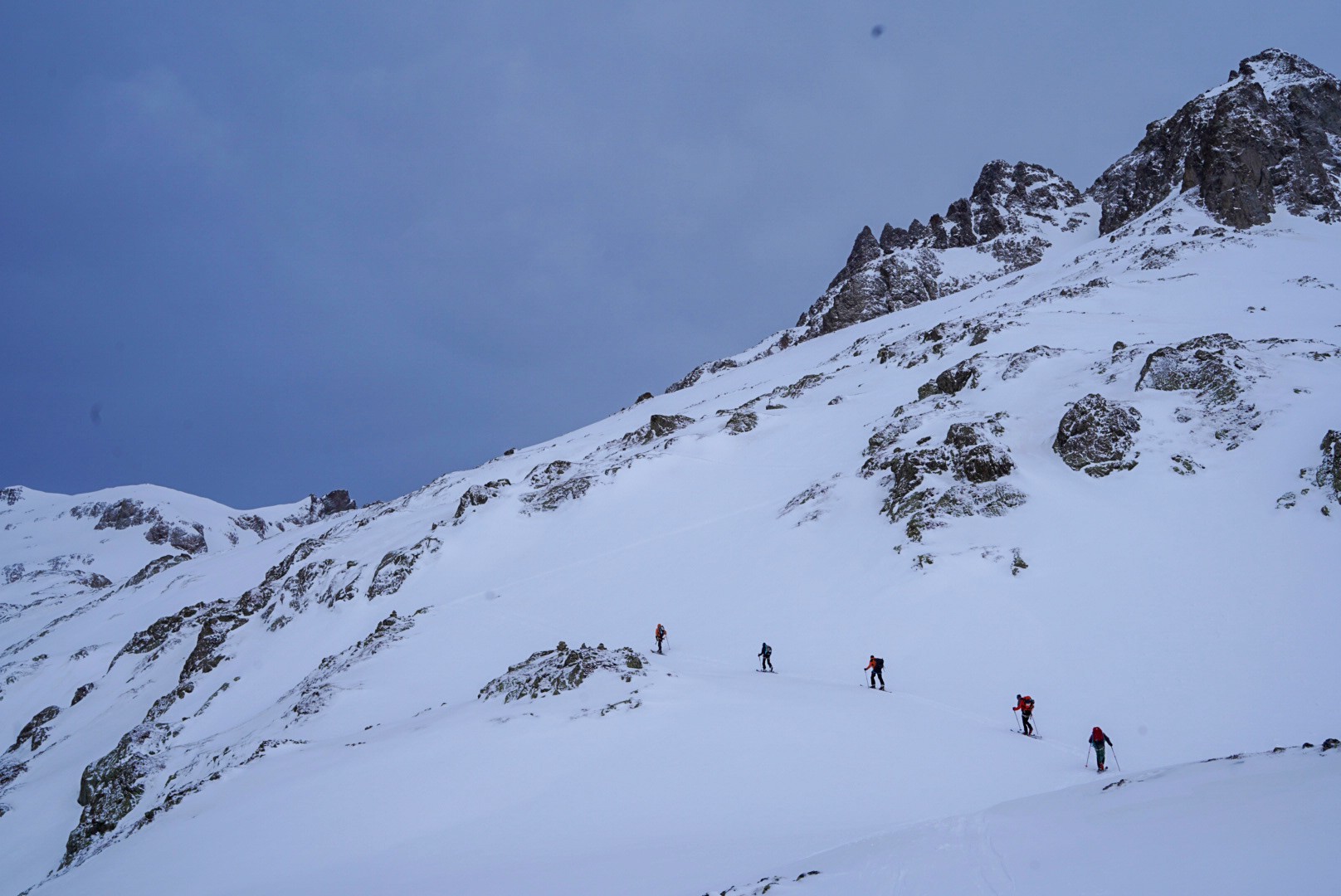 File de skieurs en montée sur un versant rocheux et enneigé, Dammastock
