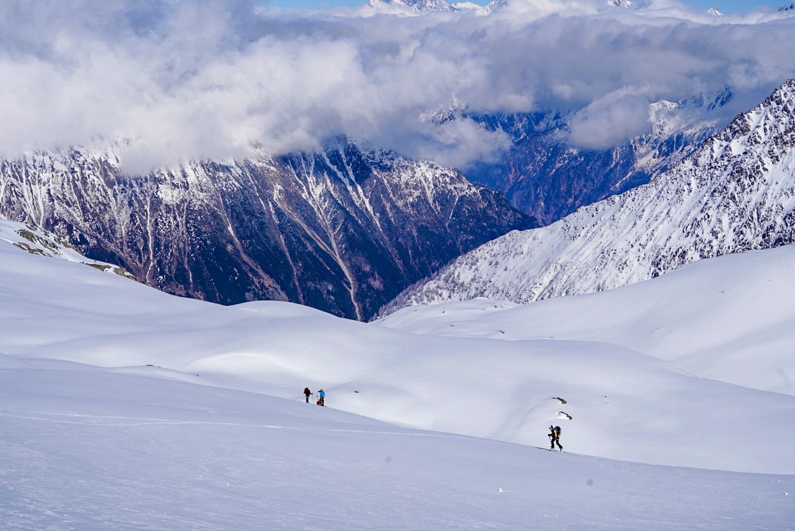 Skieurs sur un plateau de neige dominant une vallée profonde et des nuages, Dammastock