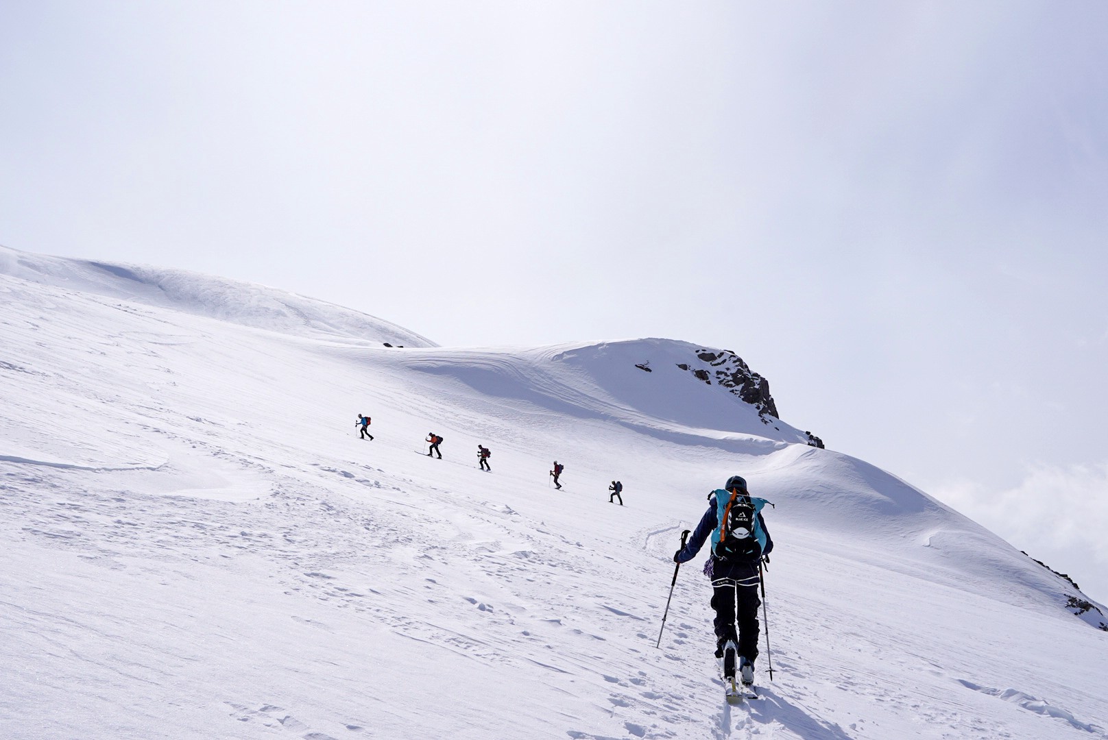 Cinq skieurs de randonnée en file sur une longue crête enneigée, traversée du Dammastock (Suisse)