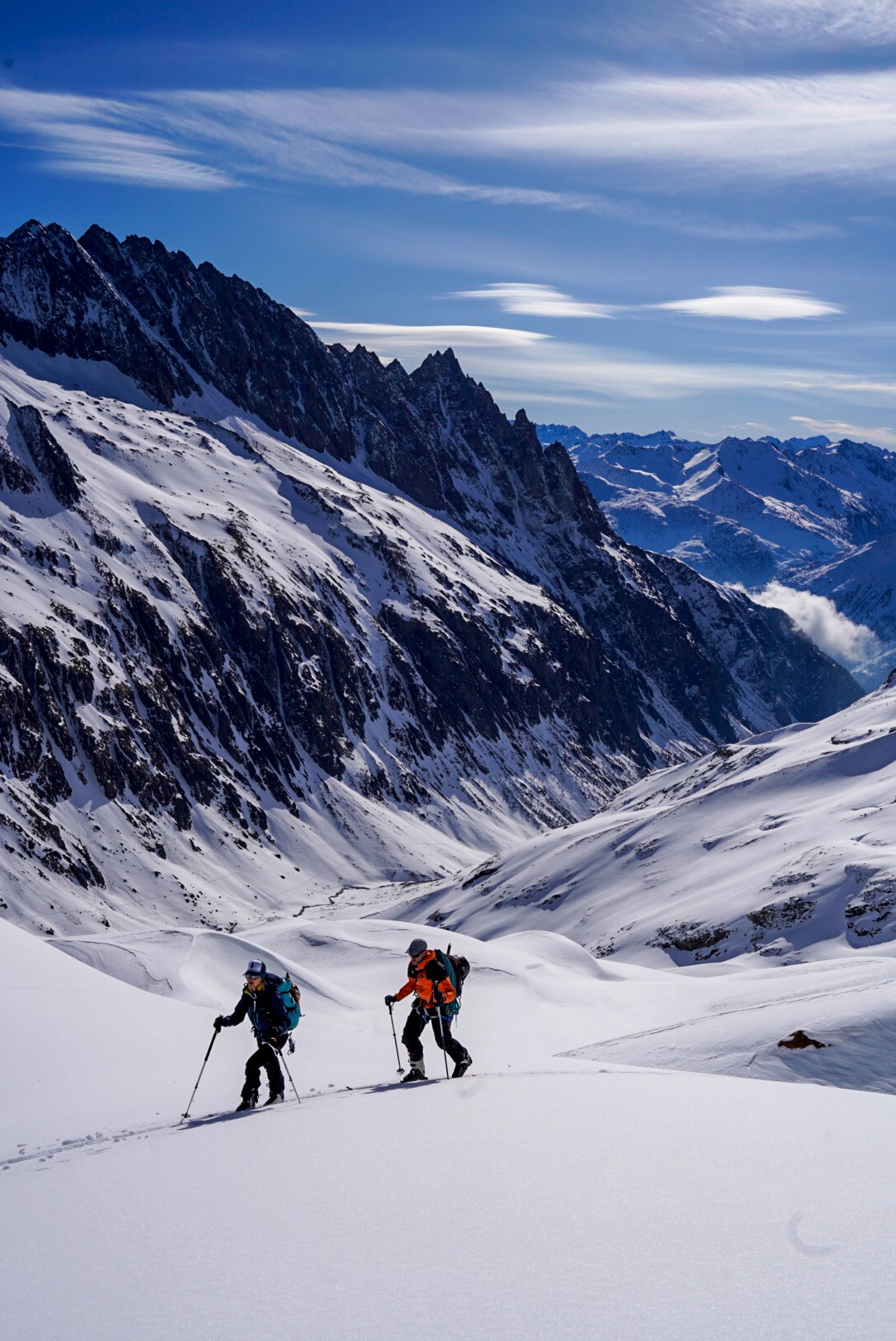 Deux skieurs en montée dans un vallon, vue plongeante sur une vallée glaciaire et des sommets, Dammastock