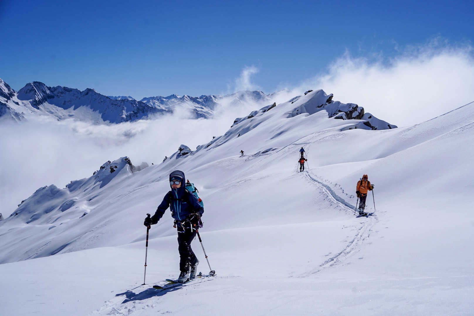 Skieur en montée sur une crête de neige, mer de nuages et sommets en arrière-plan, Dammastock