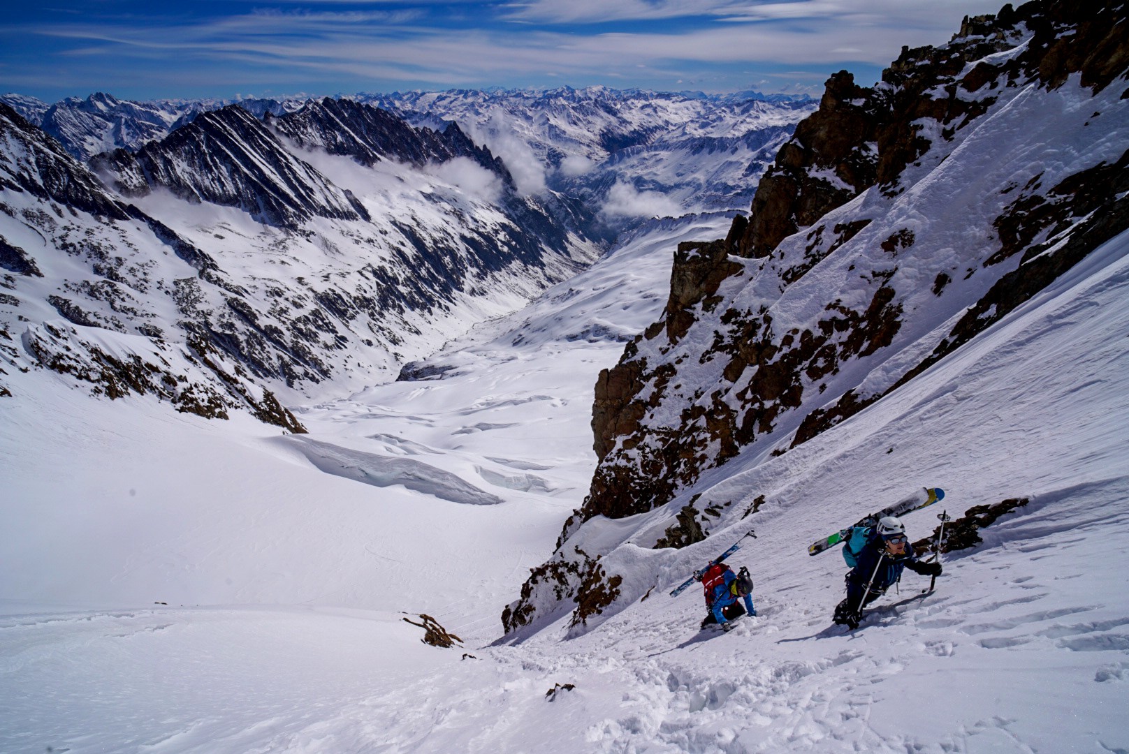 Deux skieurs grimpant à pied un couloir raide, skis sur le sac, au-dessus d'une vallée glaciaire, Dammastock