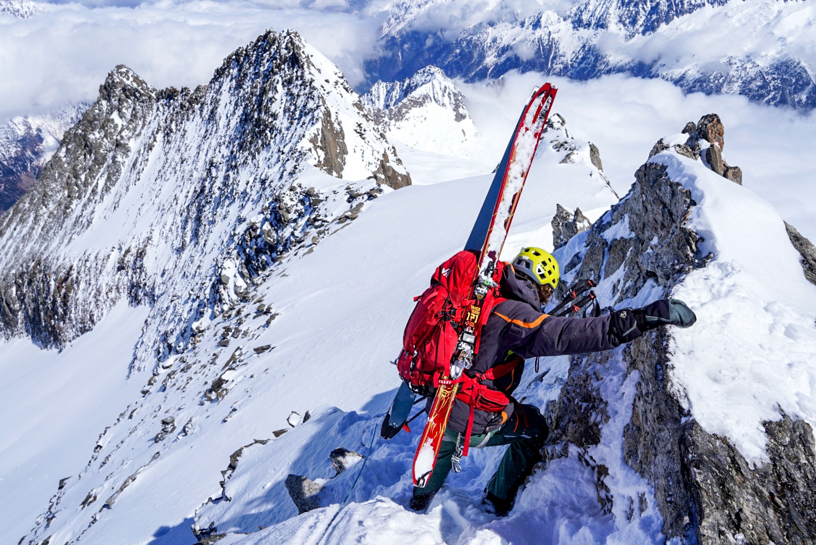 Skieur escaladant une arête rocheuse enneigée, skis rouges fixés au sac, Dammastock