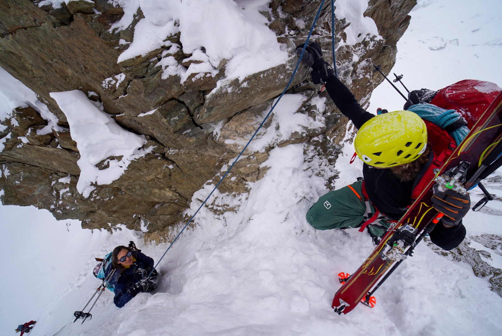 Skieur franchissant un passage rocheux raide assuré par une corde, skis sur le sac, Dammastock