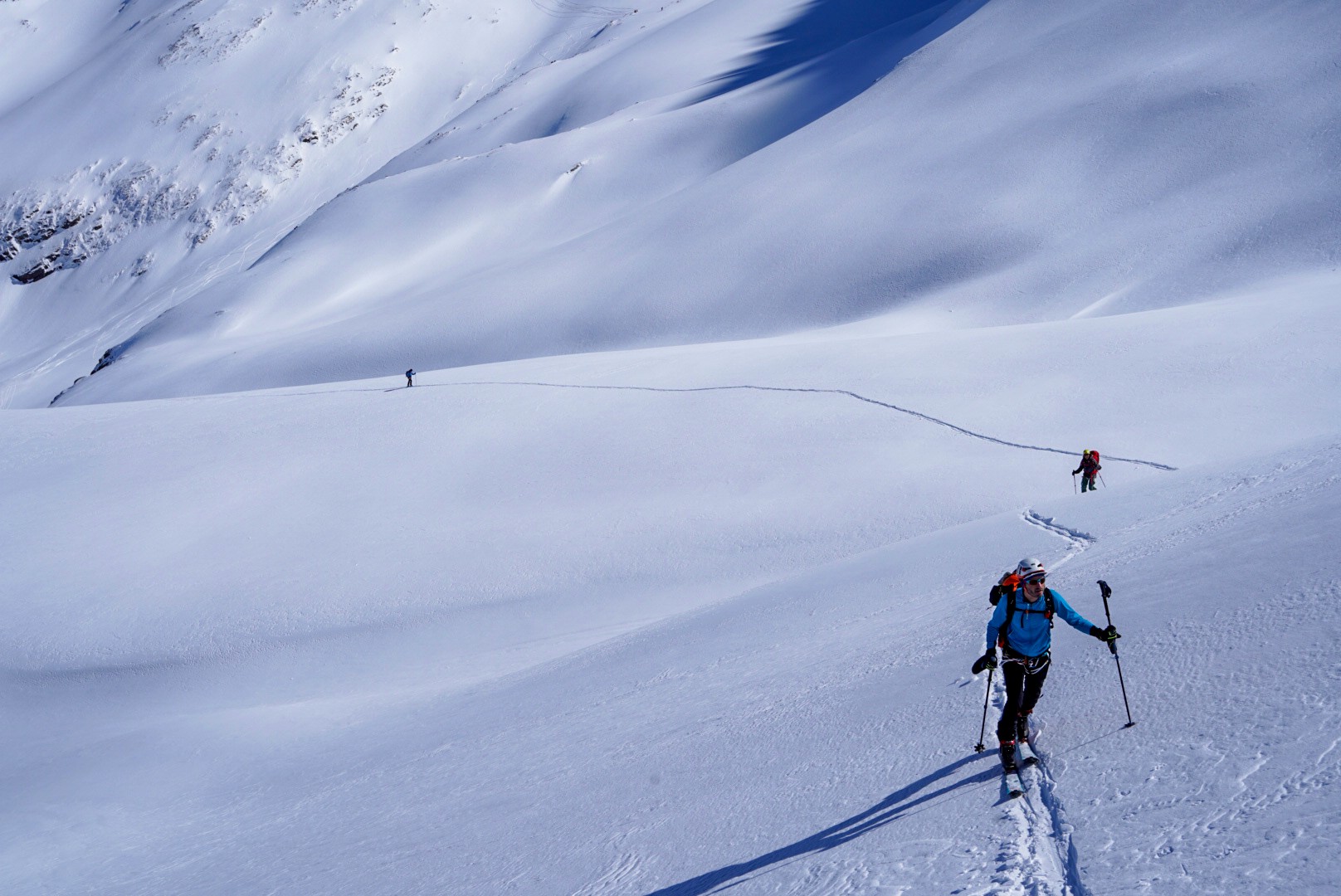 Skieur en montée sur une longue trace, cordée au loin sur un grand versant de neige, Dammastock