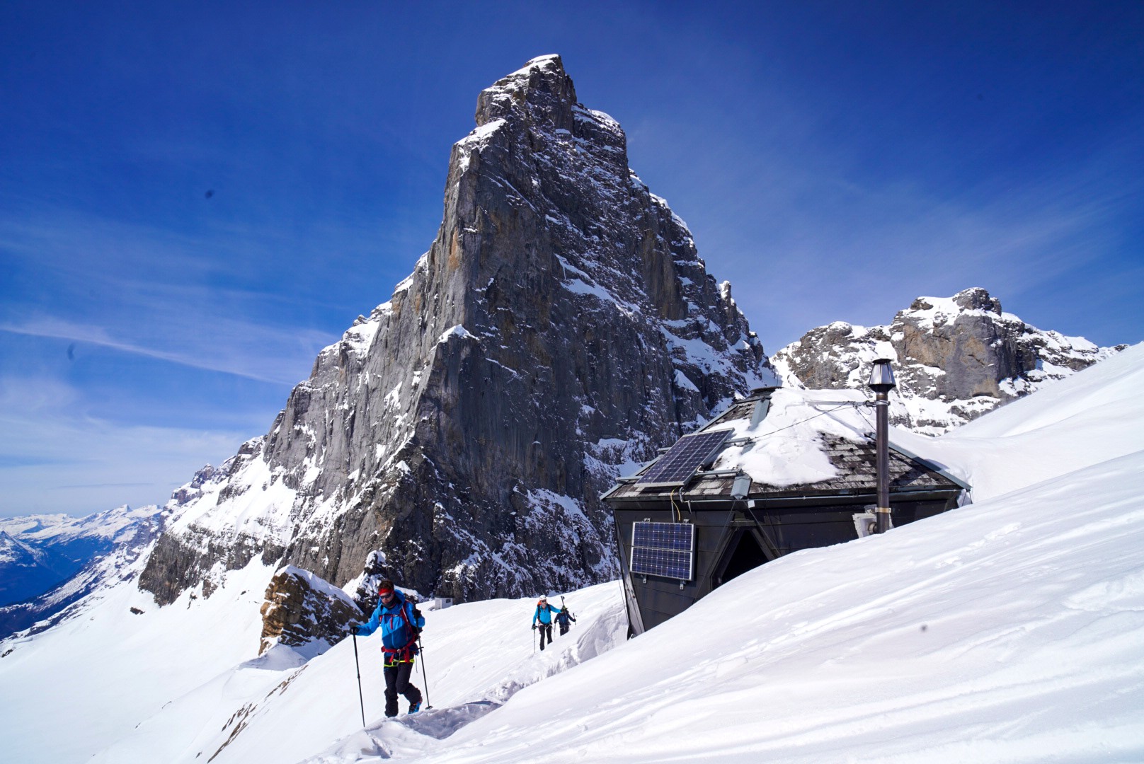 Petite cabane de bivouac sous une tour rocheuse, skieurs en approche, Dammastock