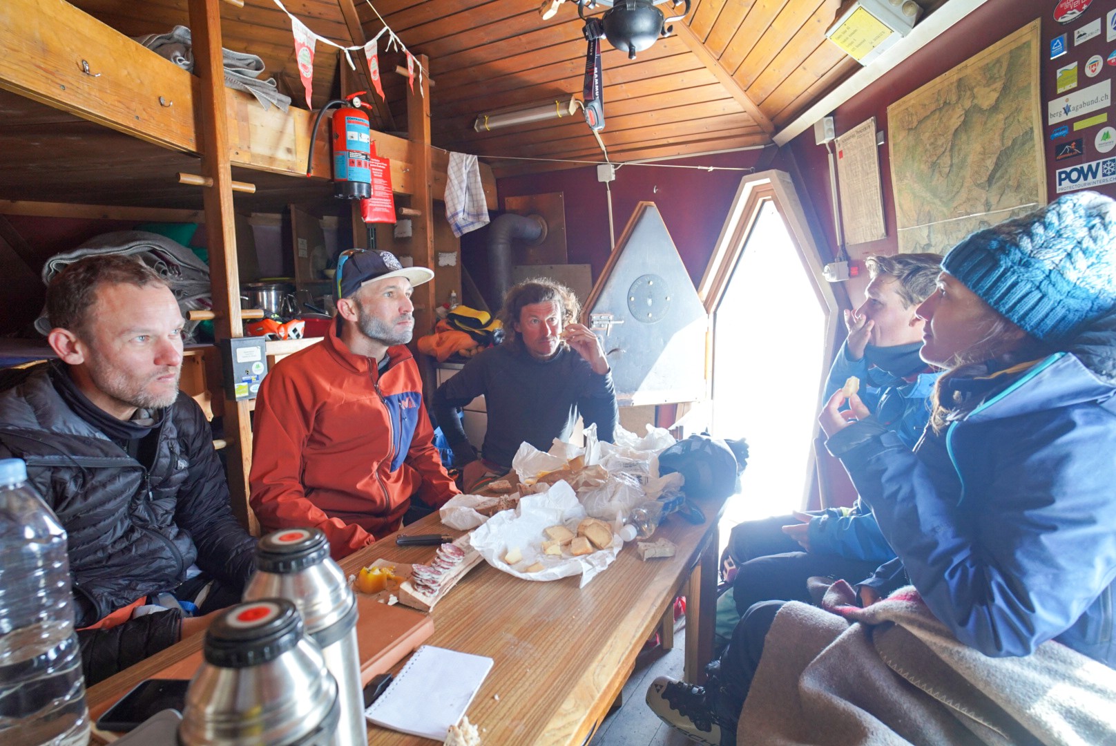 Repas de groupe dans une cabane de bois, thermos et collations sur la table