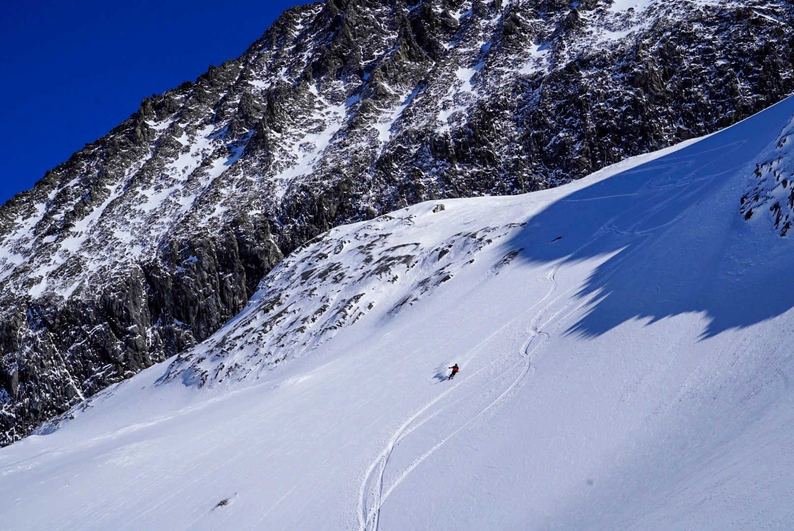 Skieur dans une pente raide sous une paroi rocheuse sombre, traces dans la neige, Dammastock