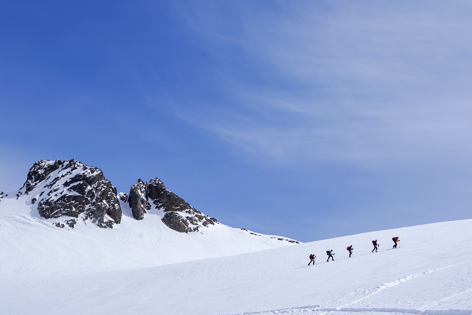 File de skieurs sur un glacier face à un sommet rocheux, ciel bleu, Dammastock