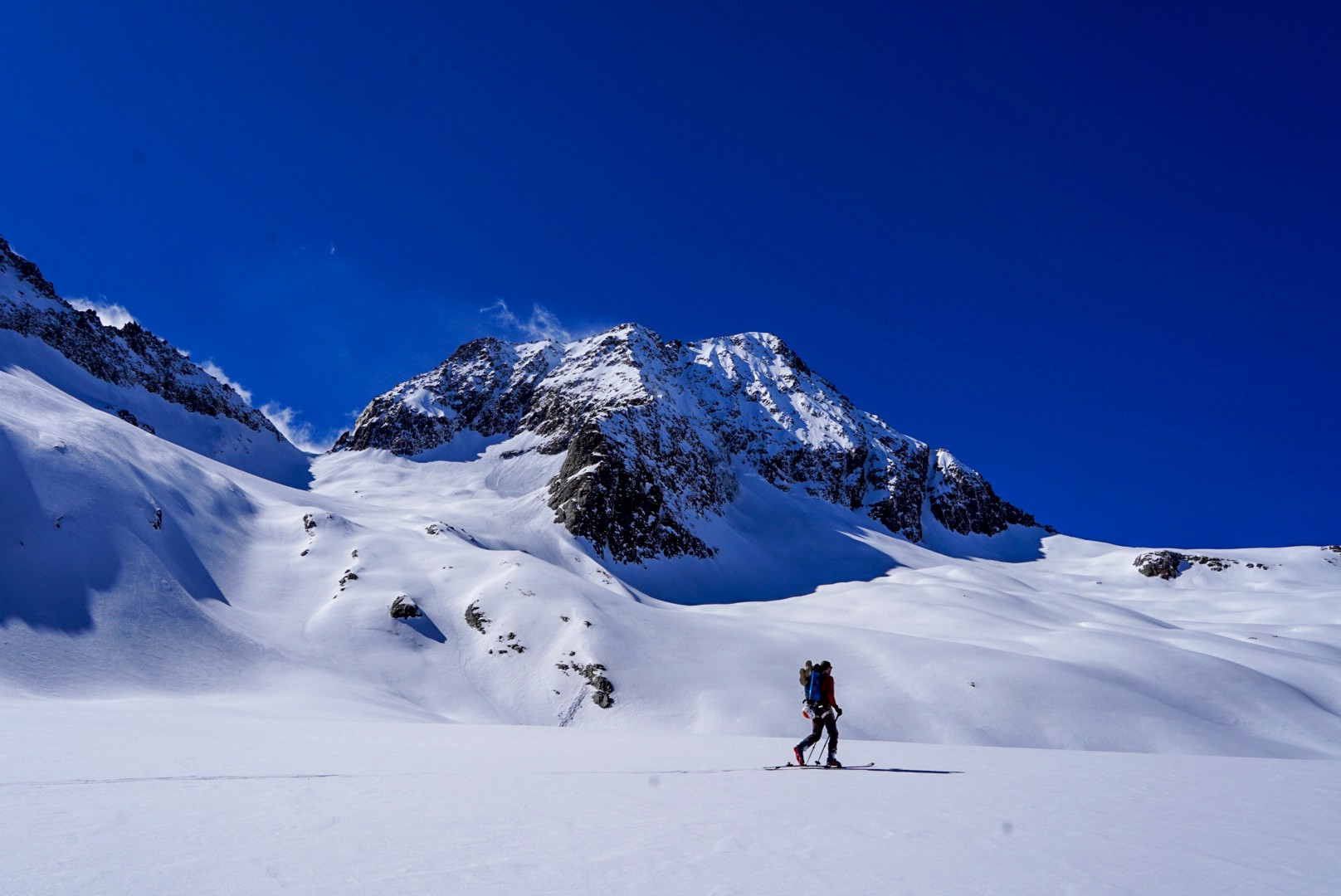 Skieur sur un plateau enneigé face à un sommet rocheux, ciel bleu profond, Dammastock
