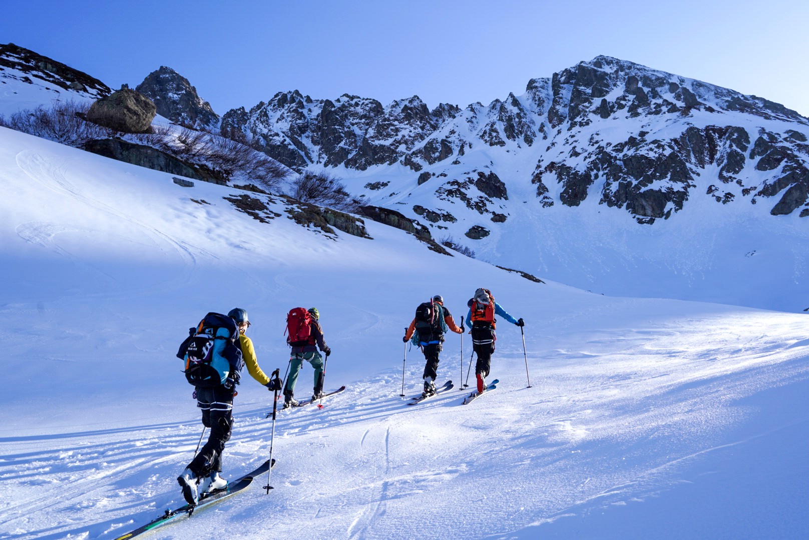 Groupe de quatre skieurs en montée dans la lumière du matin, face à un sommet rocheux, Dammastock