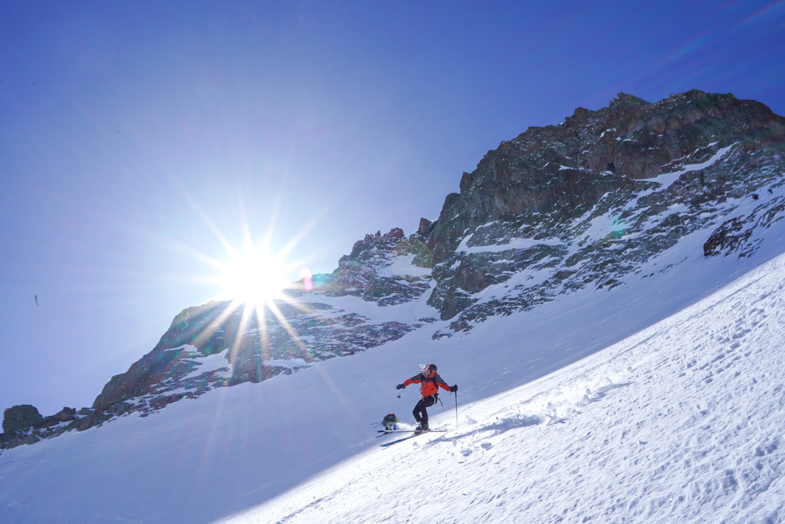 Skieur dans une pente de neige, soleil en étoile au-dessus d'une crête rocheuse, Dammastock