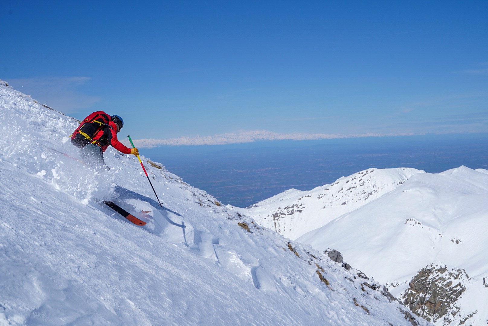 Skieur engagé dans une pente raide avec les sommets du caucase à l’horizon, vallée de Becho, vers le massif de l’Ushba, pendant le voyage à ski en Géorgie.